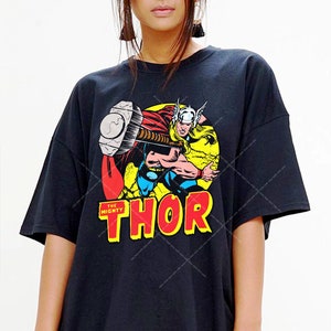 May include: Black t-shirt with a graphic of Thor, the Mighty, wielding his hammer. The text "THE MIGHTY THOR" is printed in red and yellow on the shirt.