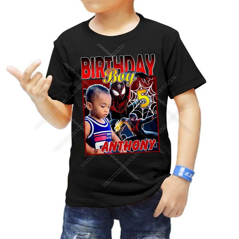 Op de afbeelding: Zwart T-shirt met een rode, gele en zwarte afbeelding van Spiderman en een kind. De tekst "Birthday Boy" staat boven de afbeelding en het nummer "5" staat rechts van de afbeelding. De tekst "Anthony" staat onder de afbeelding.