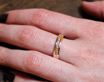 May include: A gold band ring with a row of small diamonds set in the center.