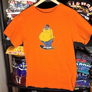 May include: A white ceramic mug with a black handle and the text "But First, Coffee" in a handwritten style. The mug is on a white surface. The mug is approximately 10 cm tall.