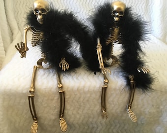 Grandes esqueletos dorados de Halloween con boa de plumas negras