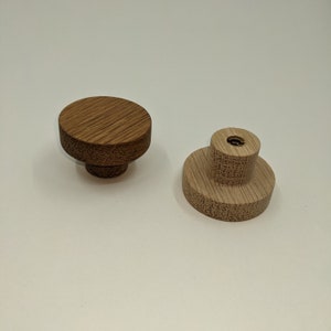 May include: Two wooden knobs, one with a dark brown finish and the other with a light brown finish. Both knobs have a round top and a cylindrical base.