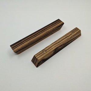 May include: Two wooden drawer pulls with a dark brown and black striped pattern. Each pull has a brass screw in the center.