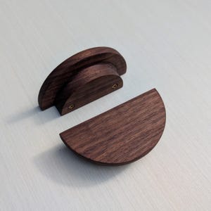 May include: Two dark brown wooden half-circle cabinet pulls with a rounded edge and a slightly raised center section. The pulls are made of solid wood and have a natural finish.