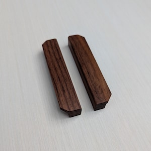 May include: Two dark brown wooden drawer pulls with a slightly angled, rectangular shape.