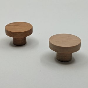May include: Two wooden knobs with a round top and a cylindrical base. The knobs are made of light brown wood.