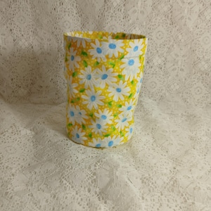 May include: A cylindrical fabric container with a bright yellow background and a pattern of white daisies with blue centers. The container is open at the top and appears to be made of a sturdy fabric.