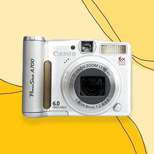 Puede incluir: Cámara digital Canon PowerShot A700 blanca con zoom óptico 6x. La cámara tiene un cuerpo plateado con un acento marrón y un flash incorporado. Cuenta con una resolución de 6.0 megapíxeles y una lente de 5.8-34.8mm.