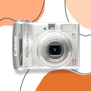 May include: A silver Canon PowerShot A560 digital camera with a 4x optical zoom lens and 7.1 megapixels. The camera has a black lens and a silver body.