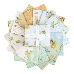 Pode incluir: Uma coleção de quadrados de tecido em várias cores pastel, com ilustrações de coelhos, flores e texto. Os quadrados de tecido estão dispostos em um padrão circular, com um pacote amarrado com uma fita no centro. O tecido é provavelmente algodão ou similar.