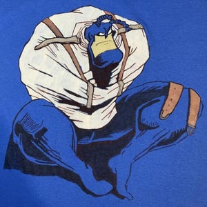May include: A blue cartoon illustration of a character wearing a white straitjacket with brown straps. The character has a blue face and a yellow beak. The background is a solid blue.