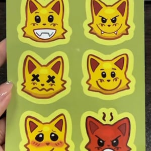 May include: A rectangular sticker sheet with a green background featuring the text JAMMER EMOTES at the top. It displays six cat-like character heads in various expressions, including happy, angry, dizzy, smiling, blushing, and furious red.