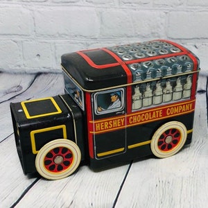 May include: A black and red toy truck with a white driver and the words "Hershey Chocolate Company" on the side. The truck is filled with miniature milk chocolate bars.