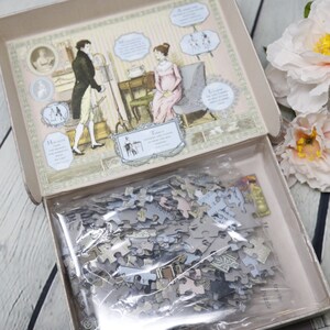 May include: A closed box with a vintage illustration of a couple in a room. The box contains a jigsaw puzzle with a similar design. The puzzle pieces are in a plastic bag.
