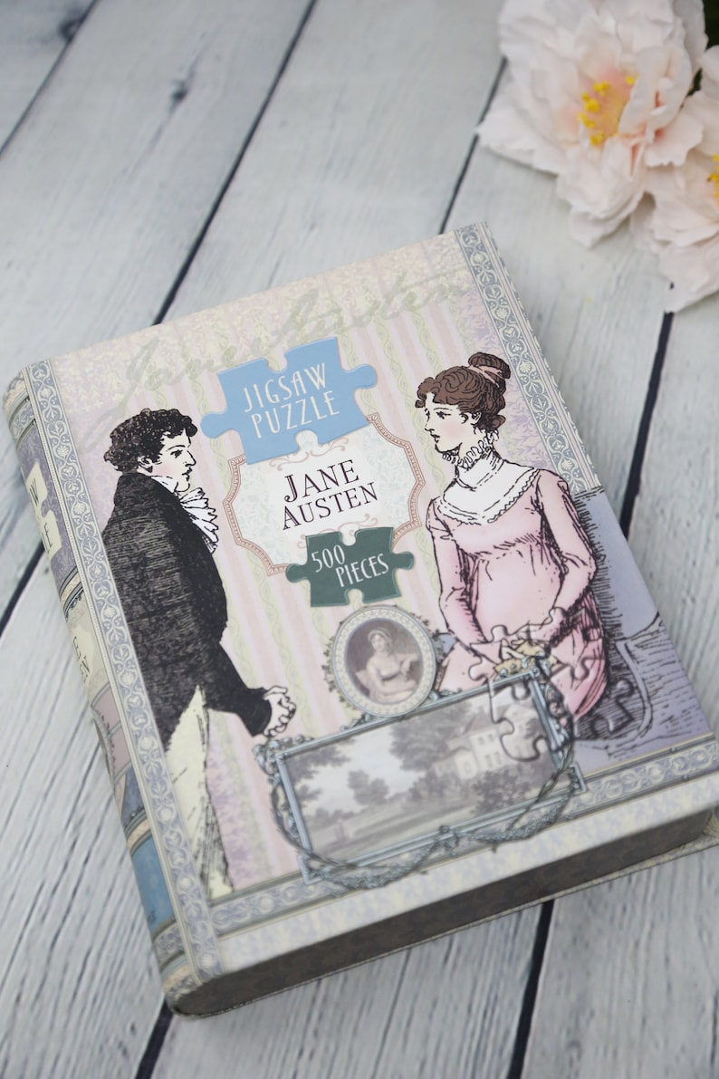 May include: A vintage-style jigsaw puzzle box featuring a couple in period clothing. The box is decorated with a floral pattern and the text "Jigsaw Puzzle Jane Austen 500 Pieces".