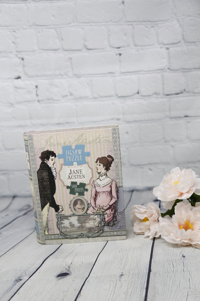May include: A vintage-style jigsaw puzzle box featuring a couple in period clothing. The box is decorated with a pink and white striped pattern and the text "Jigsaw Puzzle Jane Austen 500 Pieces".