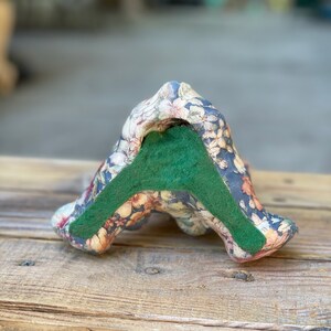May include: A floral patterned ceramic bookend with a green felt bottom. The bookend is shaped like a stylized letter A.
