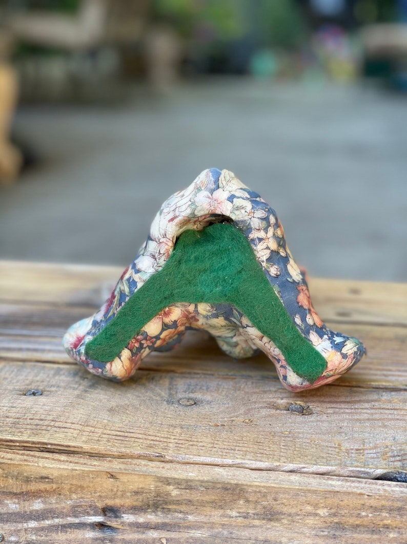 May include: A floral patterned ceramic bookend with a green felt bottom. The bookend is shaped like a stylized letter A.