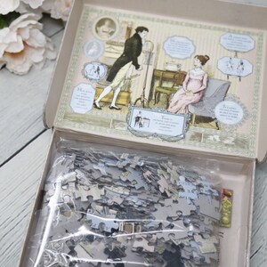 May include: A vintage-style jigsaw puzzle in a box with a colorful illustration of a couple in a room. The box lid is open and the puzzle pieces are visible inside a plastic bag. The text on the box reads "How quick you must be to appreciate what we like!"