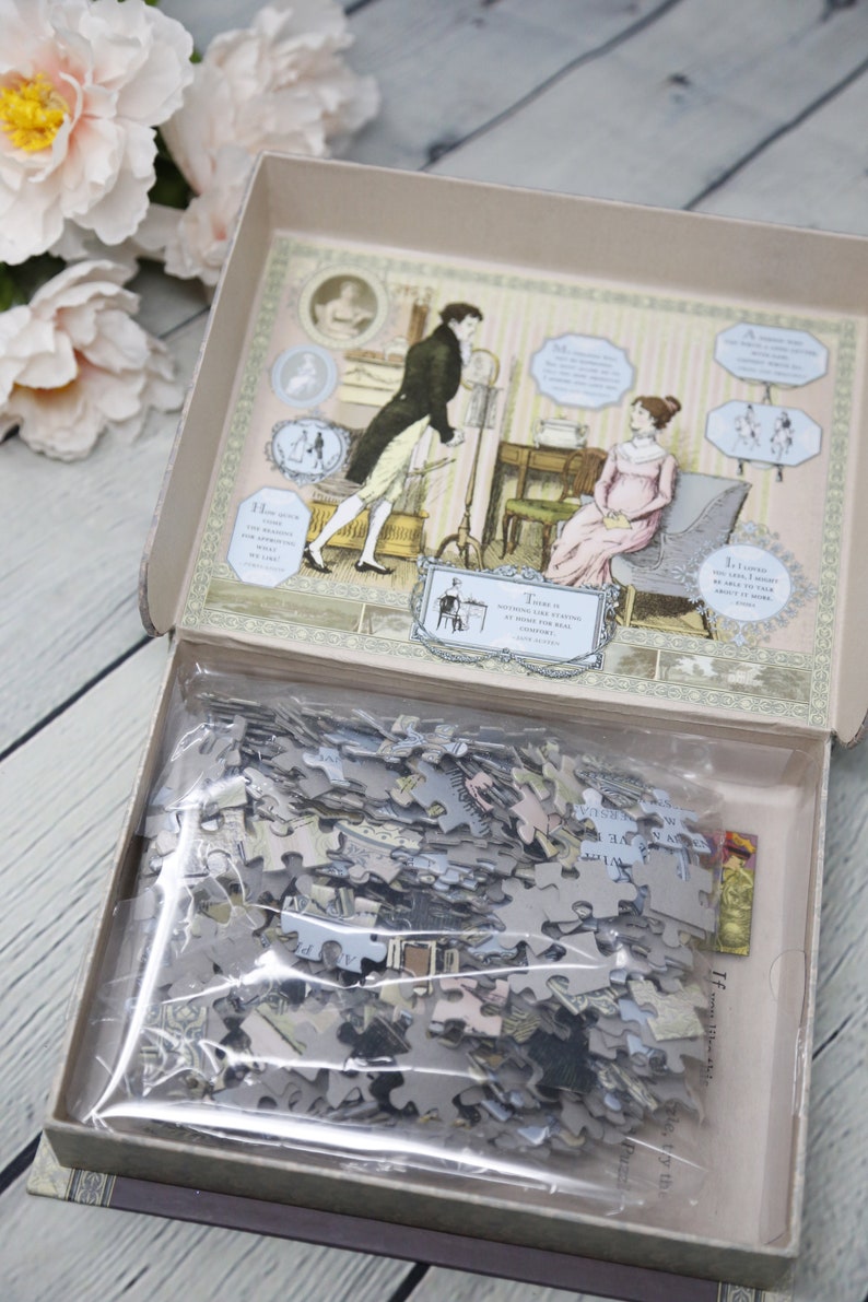 May include: A vintage-style jigsaw puzzle in a box with a colorful illustration of a couple in a room. The box lid is open and the puzzle pieces are visible inside a plastic bag. The text on the box reads "How quick you must be to appreciate what we like!"