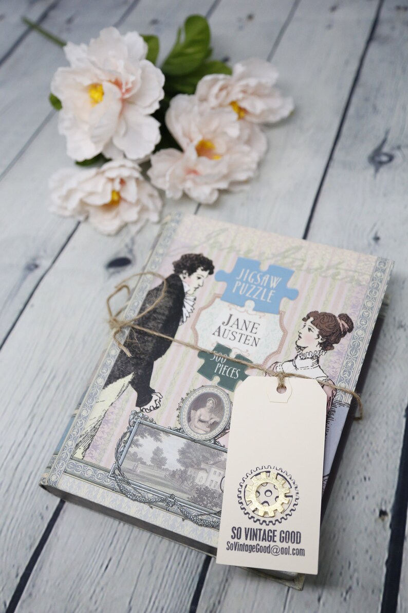 May include: A vintage-style jigsaw puzzle featuring a scene from Jane Austen's novel, with a 500-piece count. The puzzle is packaged in a box with a cream background and a blue and white striped pattern. A brown twine bow is tied around the box, and a cream-colored tag with a gold gear design is attached. The tag reads "So Vintage Good" and includes a website address.