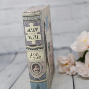 May include: A book-shaped box with a jigsaw puzzle design. The box is decorated with a floral pattern and the text "Jigsaw Puzzle" and "Jane Austen".