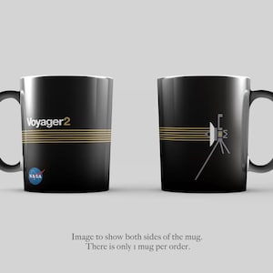 Puede incluir: Taza de café de cerámica negra con un diseño de rayas doradas y el texto "Voyager 2" en un lado. El otro lado presenta una ilustración estilizada de la nave espacial Voyager 2. El logotipo de la NASA es visible en la taza.