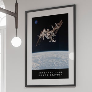 Può includere: Un poster in bianco e nero con una foto della Stazione Spaziale Internazionale in orbita attorno alla Terra. Il poster presenta il logo della NASA e il testo "INTERNATIONAL SPACE STATION" in basso.