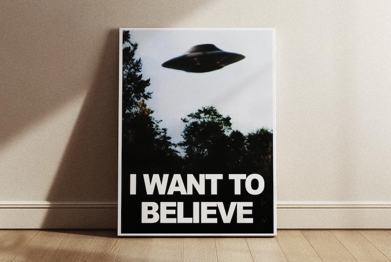 May include: A black and white poster with a photo of a flying saucer in the sky above a forest. The text "I WANT TO BELIEVE" is printed in white letters on a black background.
