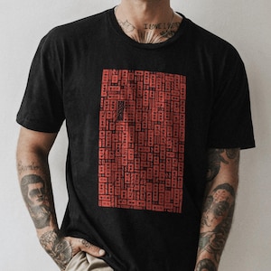 May include: Black t-shirt featuring a red geometric design. The design is composed of various rectangular and square shapes, creating a complex pattern. The shirt is made of a soft material and has a classic crew neck.