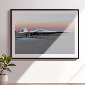 May include: A white and blue experimental aircraft with a long, narrow wingspan sits on a runway. The aircraft has a red and white logo on the tail.