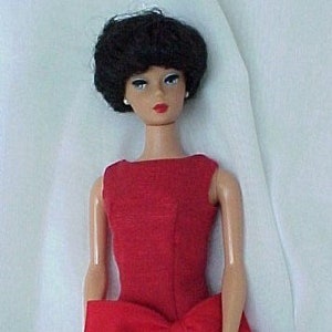 May include: A red and blue doll dress with a large red bow. The dress has a red bodice and a blue skirt with white polka dots.