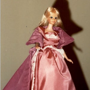Pode incluir: Uma boneca Barbie vintage vestindo um vestido de cetim rosa com uma borda de renda branca e uma capa de veludo rosa combinando.