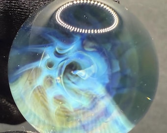 May include: A clear glass marble with blue and white swirls inside. The marble has a silver ring around the center.