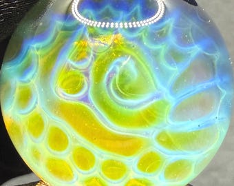 May include: A circular glass pendant featuring a swirling pattern of translucent lime green and vibrant yellow hues, overlaid with a delicate, web-like network of iridescent light blue lines that create a textured, organic appearance.