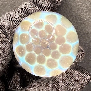 Könnte beinhalten: Eine klare Glaskugel mit einem wirbelnden Muster aus braunen und weißen Punkten. Die Kugel hat einen blauen, irisierenden Schimmer.