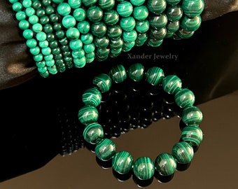 Puede incluir: Una pila de pulseras de malaquita verde con una sola pulsera colocada debajo. Las pulseras están hechas de cuentas redondas con un patrón rayado. El texto "Xander Jewelry" y "Malachite Bracelet" es visible en la imagen.
