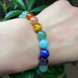 May include: A beaded bracelet featuring a sequence of smooth, polished spherical stones in various colors including red, orange, yellow, green, light blue, dark blue, and purple, arranged in a single strand on an elastic cord.