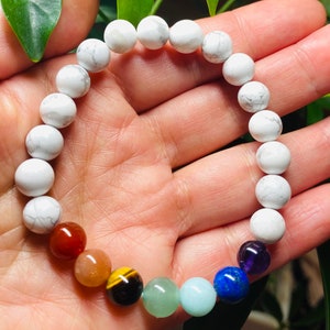 May include: A stretch bracelet composed of round white howlite beads with grey veining, accented by a sequence of seven smooth, polished gemstone beads in red, orange, yellow, green, light blue, dark blue, and deep purple colors.