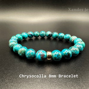 Può includere: Un braccialetto di crisocolla turchese con perline da 8 mm. Il braccialetto presenta una perlina distanziatrice color oro. I testi "Xander Jewelry" e "Chrysocolla 8mm Bracelet" sono visibili.