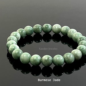 Könnte beinhalten: Ein grünes Jadearmband mit runden Perlen. Das Armband liegt auf einer schwarzen reflektierenden Oberfläche. Der Text "Xander Jewelry" und "Burmese Jade" ist unterhalb des Armbands sichtbar.