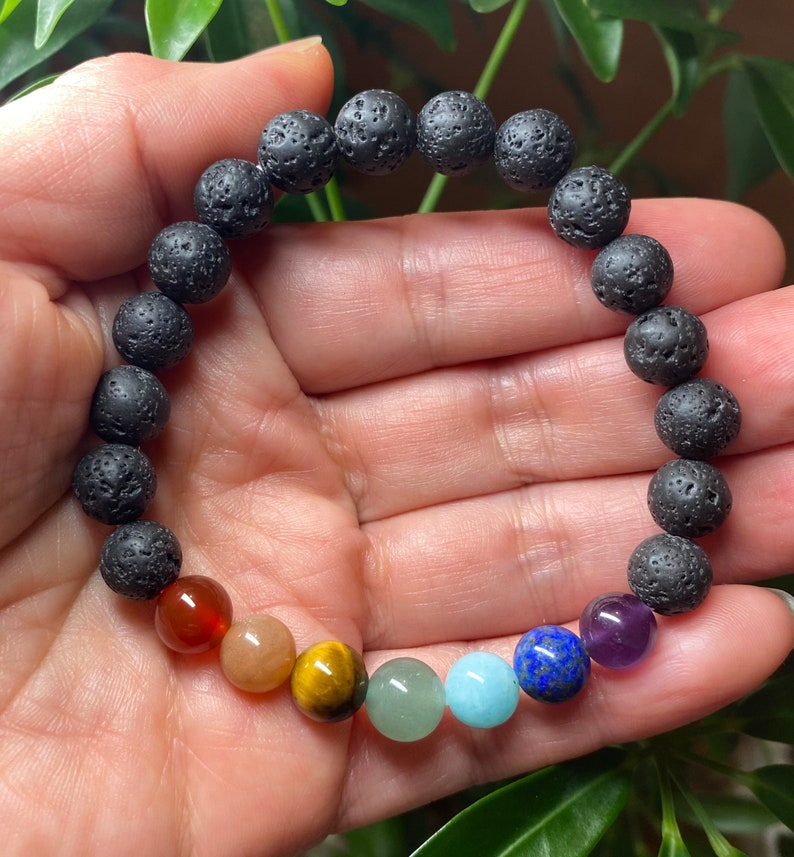 May include: A beaded bracelet featuring a series of porous, black lava stone beads and seven smooth, polished gemstone beads in a spectrum of colors including red, orange, yellow, green, light blue, dark blue, and purple, arranged in a circular row.