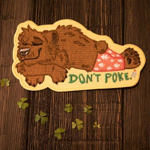 Op de afbeelding: Geborduurde patch met een bruine beer in pyjama, liggend met gesloten ogen. De patch heeft een gele rand en de tekst "DON'T POKE" in groen. De pyjama van de beer is rood met witte sterpatronen.