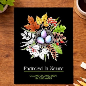 K&ouml;nnte beinhalten: Schwarzes Cover eines Malbuchs mit dem Titel "Encircled In Nature". Das Cover zeigt eine detaillierte Illustration eines Vogelnests mit drei gesprenkelten Eiern, umgeben von bunten Bl&auml;ttern und Beeren. Das Buch ist von Ellie Marks.