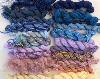 May include: Assortment of colorful embroidery floss in various shades of blue, purple, pink, and yellow. The floss is arranged in rows, with each row containing a different color.