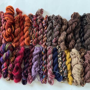 May include: A collection of 18 skeins of yarn in various shades of brown, red, purple, and blue. The yarn is arranged in rows and is ready to be used for knitting or crocheting.