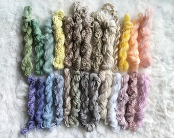 May include: A collection of 28 skeins of embroidery floss in a variety of pastel colors, including green, blue, yellow, pink, and white.