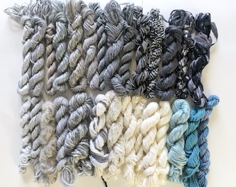 May include: Assortment of yarn skeins in various shades of gray, white, and blue. The yarn is arranged in rows, with the darkest shades at the top and the lightest shades at the bottom.
