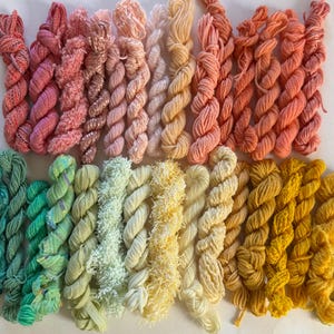 May include: An assortment of colorful yarn skeins in shades of pink, peach, green, yellow, and gold. The yarn is arranged in neat rows, showcasing a variety of textures and hues. Ideal for knitting, crochet, or other fiber art projects.