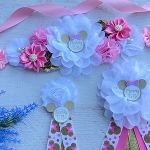 May include: Pink and white flower sash with gold glitter Mickey Mouse ears and the text "Mommy to Be".  Two additional sashes with white flowers and gold glitter Mickey Mouse ears with the text "Mommy to Be" and "Daddy to Be".